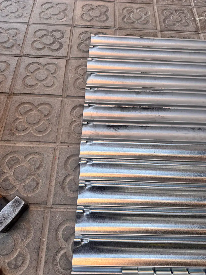 Lamas nuevas de persiana metálica extendidas sobre el panot de una calle de Barcelona antes de montarlas